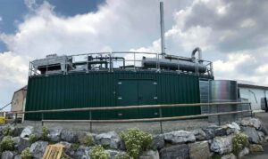 Grüner BHKW-Container mit Kühlern und Geländer auf einer Natursteinmauer