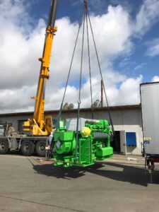Kran hebt ein grünes Jenbacher-BHKW-Modul von einem Lastwagen