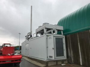 Weißer BHKW-Container mit Kühlern auf dem Dach an einer Biogasanlage