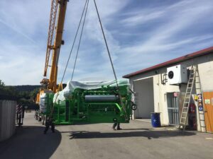 Kran hebt ein grünes Jenbacher-Motormodul auf einem Hof