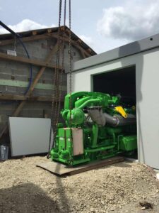 Grünes BHKW-Modul wird mit dem Kran in ein Betongebäude gesetzt