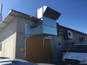 Gebäude mit großem silbernen Lüftungskanal über einer Holztür
