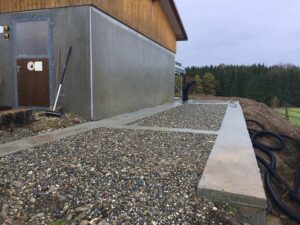 Verkleidetes Betriebsgebäude mit Kiesfläche und Betonfundament am Feldrand