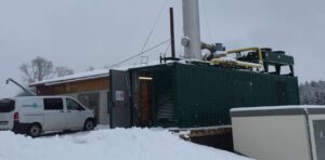 Grüner BHKW-Container mit Schornstein im Schnee, davor ein Transporter