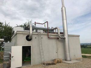 BHKW-Betongebäude mit offener Tür, Leiter und hohem Schornstein