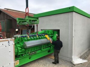 Grüner Jenbacher-Motor wird am Kranhaken in ein Betongebäude eingeführt