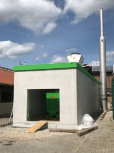 Betongebäude mit grünem Dachrand, offener Öffnung und hohem Schornstein