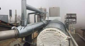 Isolierte Abgasleitungen auf dem Dach eines BHKW-Gebäudes im Nebel