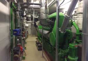 Maschinenraum mit grünem Jenbacher-Motor, Pumpen und isolierten Leitungen