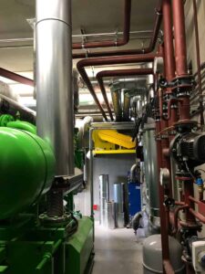 Maschinenraum mit grünem Motor, Abgasrohr und roten Rohrleitungen