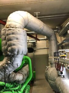 Isolierte Abgasleitungen über einem grünen Motor im Maschinenraum