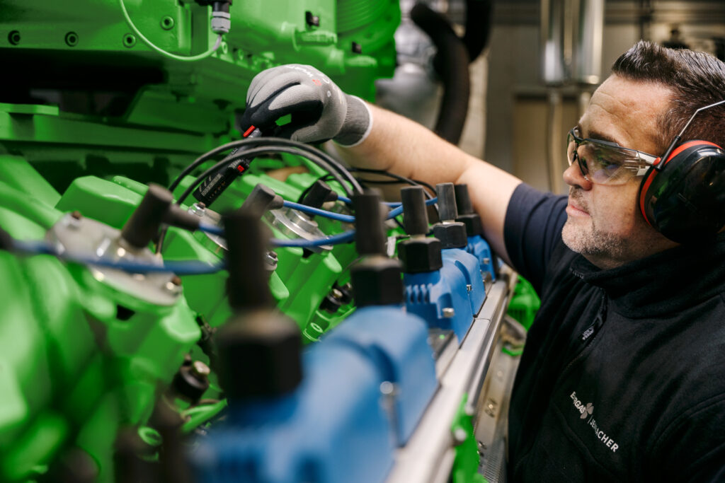 Mann mit Schutzbrille und Gehörschutz arbeitet an Kabeln eines grünen Motors