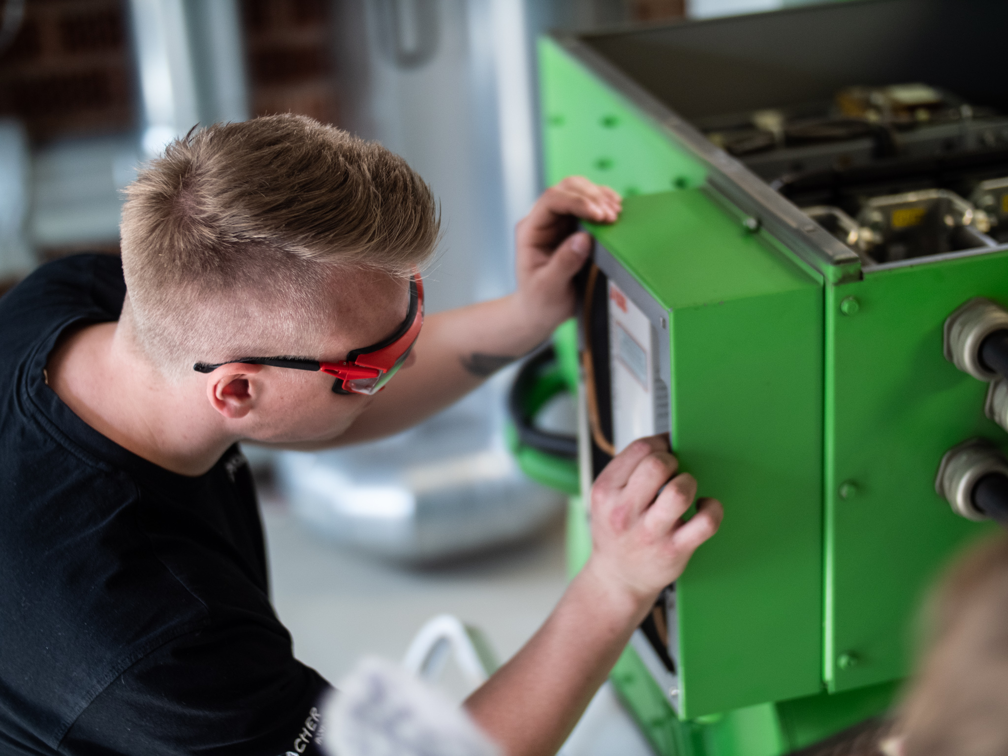 Mann mit Schutzbrille arbeitet an einem geöffneten grünen Schaltkasten