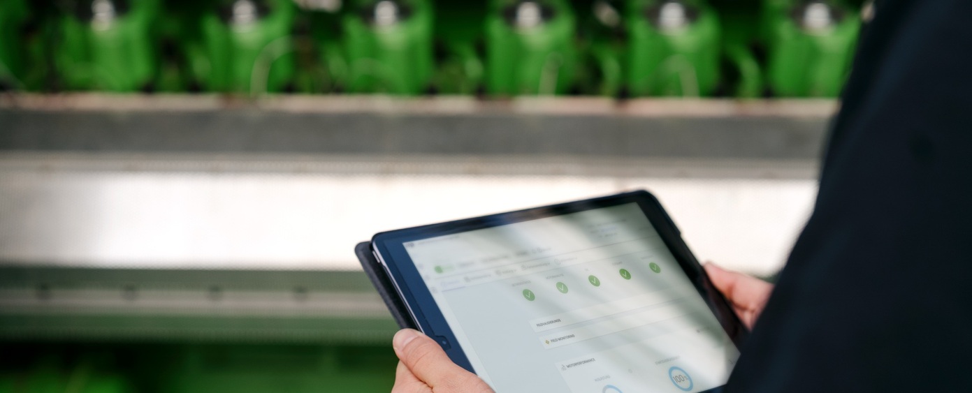 Hände halten ein Tablet mit Statusanzeige vor einem grünen Motor
