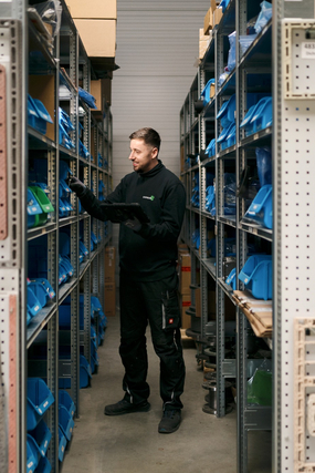 Mann in Arbeitskleidung in einem schmalen Regalgang mit blauen Behältern