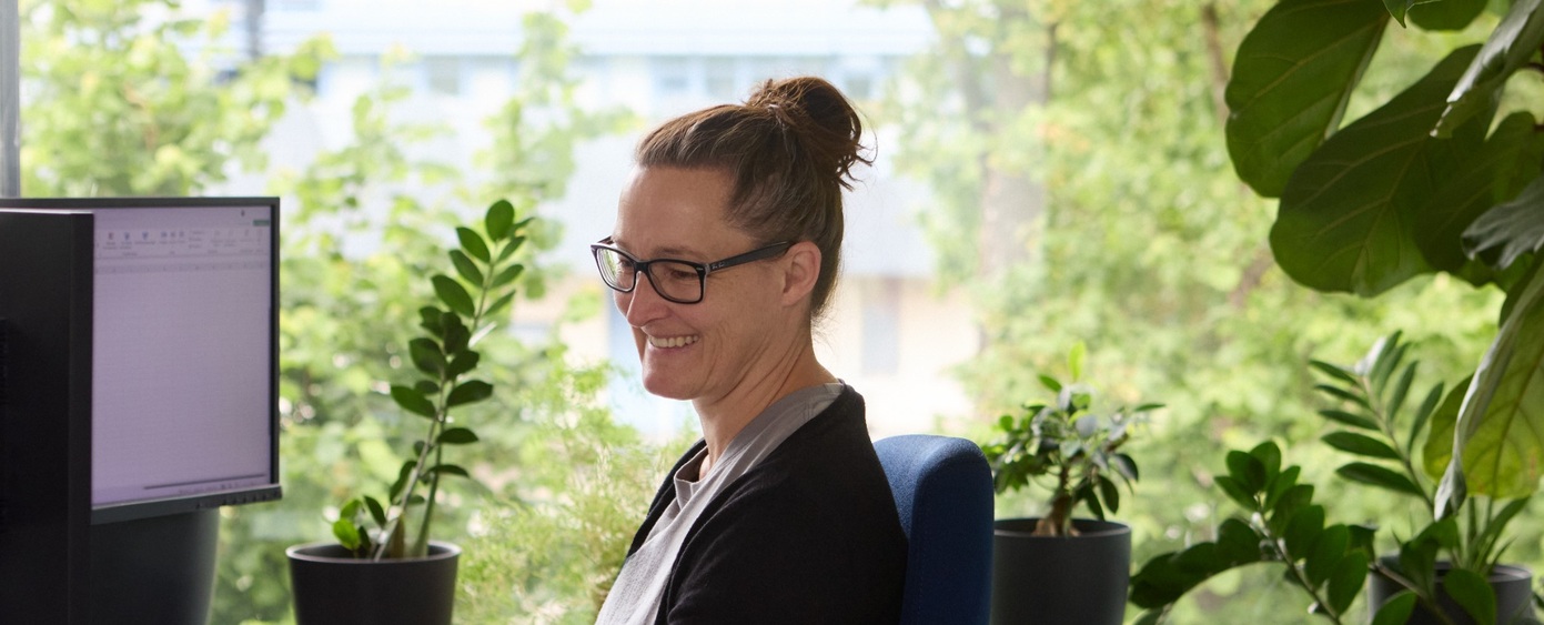 Frau mit Brille arbeitet am Computer, umgeben von Grünpflanzen