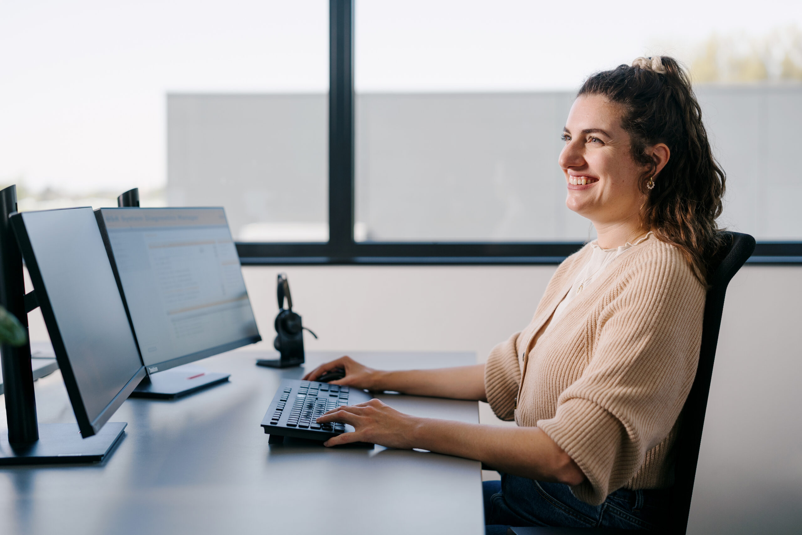 Lächelnde Frau mit Locken arbeitet an einem Computerarbeitsplatz
