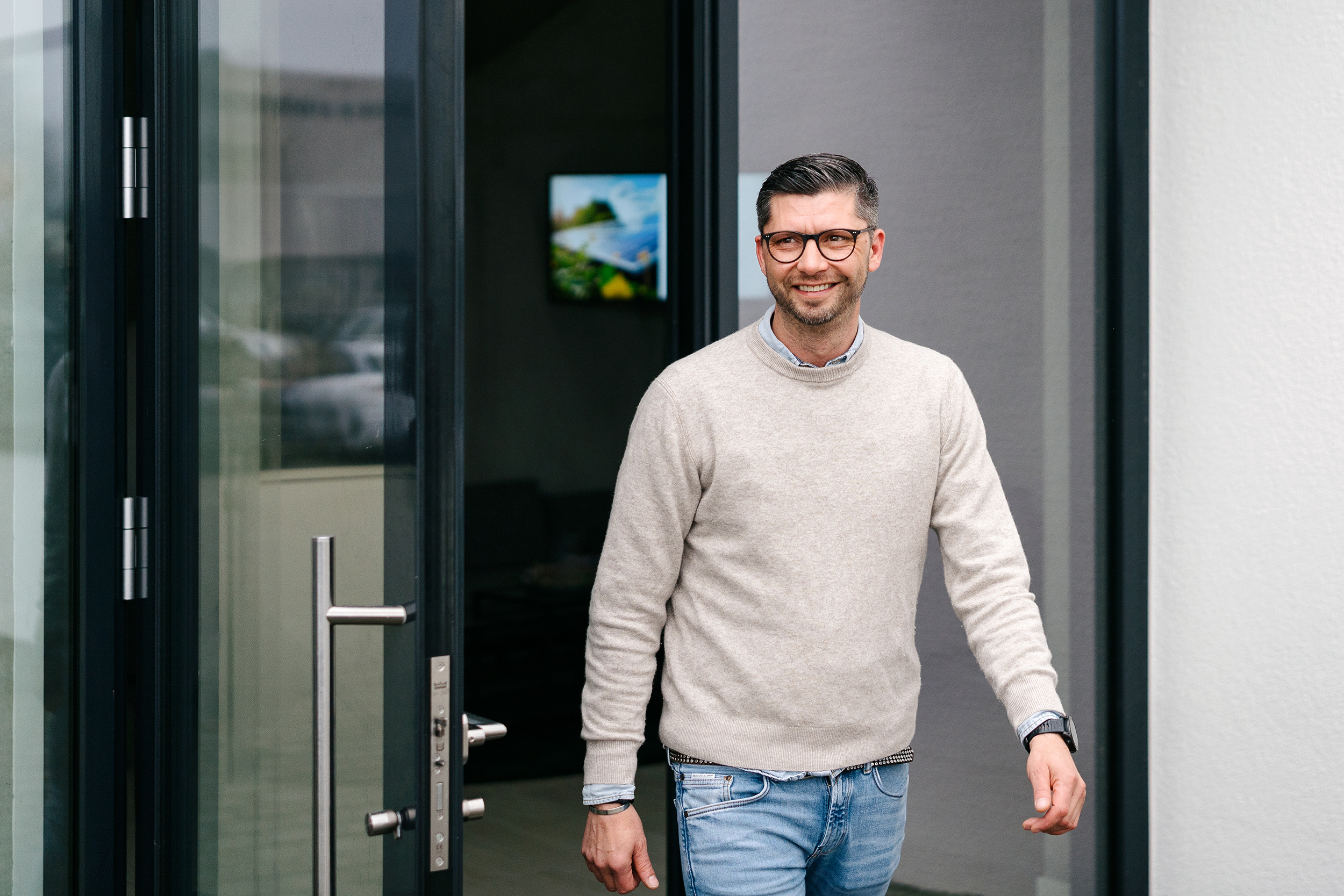 Lächelnder Mann mit Brille kommt durch eine Glastür