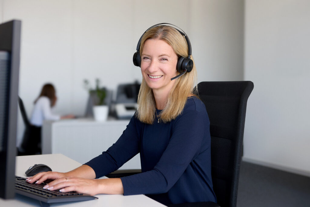 Lächelnde Frau mit Headset arbeitet am Computer im Büro