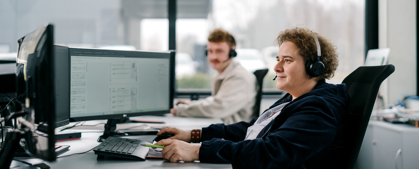 Zwei Personen mit Headset arbeiten an Bildschirmarbeitsplätzen