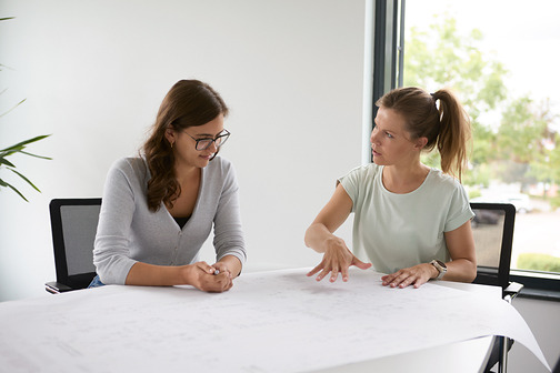 Zwei Frauen besprechen einen ausgebreiteten Plan am Tisch